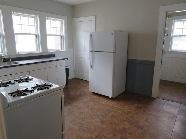 kitchen featuring a wainscoted wall, white appliances, a sink, white cabinets, and dark countertops