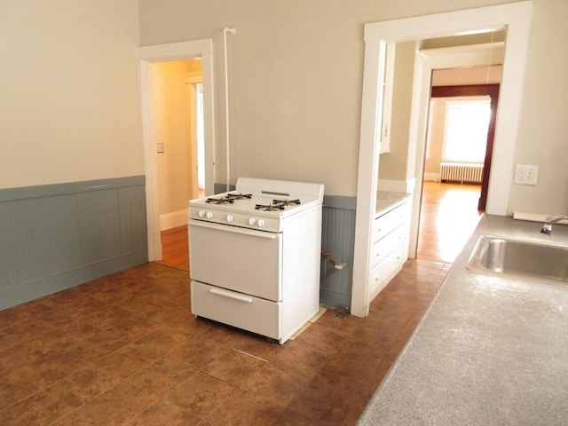 kitchen with radiator, white range with gas stovetop, a sink, and wainscoting