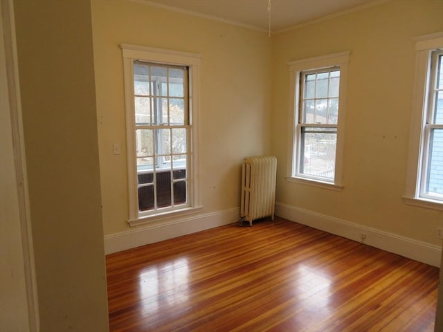 empty room featuring a healthy amount of sunlight, radiator heating unit, crown molding, and wood finished floors