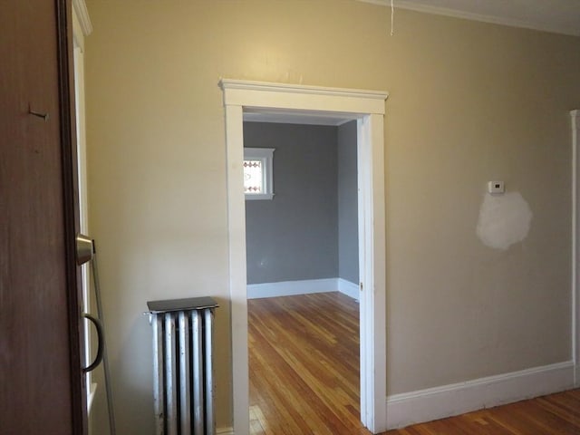 hallway featuring baseboards, radiator heating unit, and wood finished floors