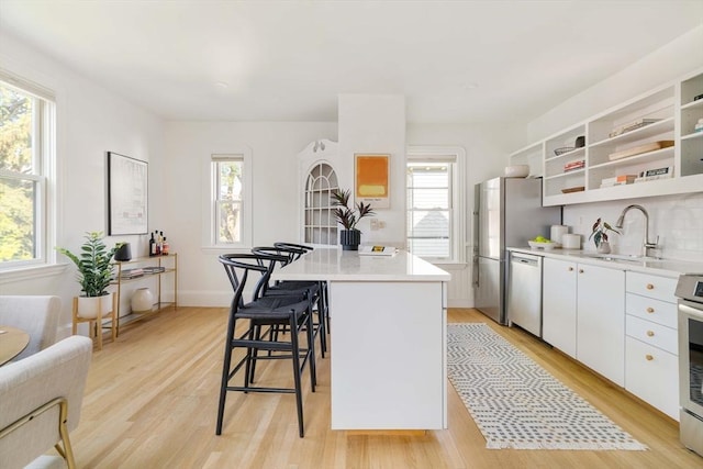 31 Kidder Ave Unit 31, Somerville, MA 02144 - kitchen with stainless steel appliances, a sink, a breakfast bar, light wood-style flooring, and white cabinetry