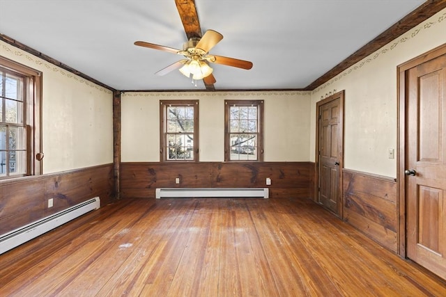 empty room featuring baseboard heating, ceiling fan, wooden walls, and hardwood / wood-style floors