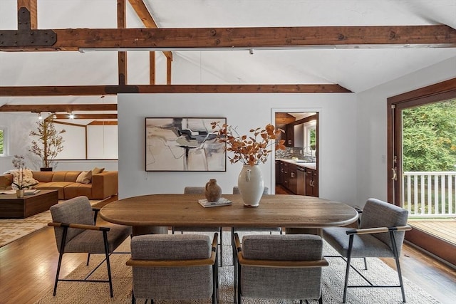 dining space featuring light wood-style floors and vaulted ceiling with beams