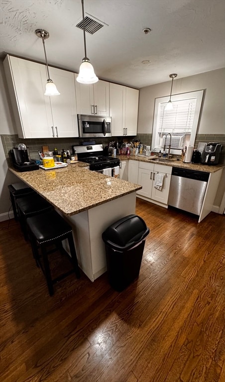 kitchen with decorative light fixtures, white cabinetry, a breakfast bar area, and appliances with stainless steel finishes