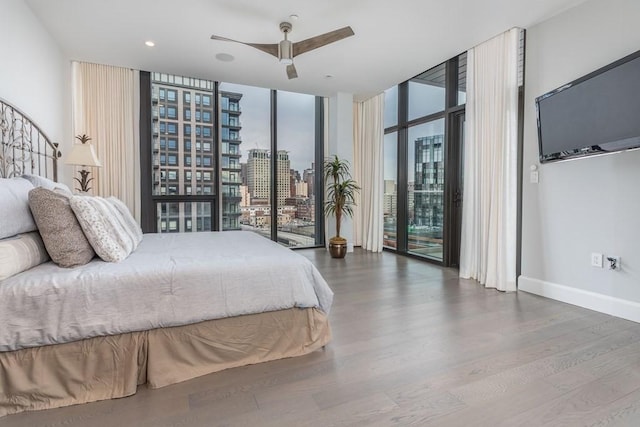 bedroom with multiple windows, a wall of windows, wood finished floors, and access to exterior