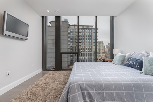 bedroom featuring a view of city, expansive windows, wood finished floors, and baseboards