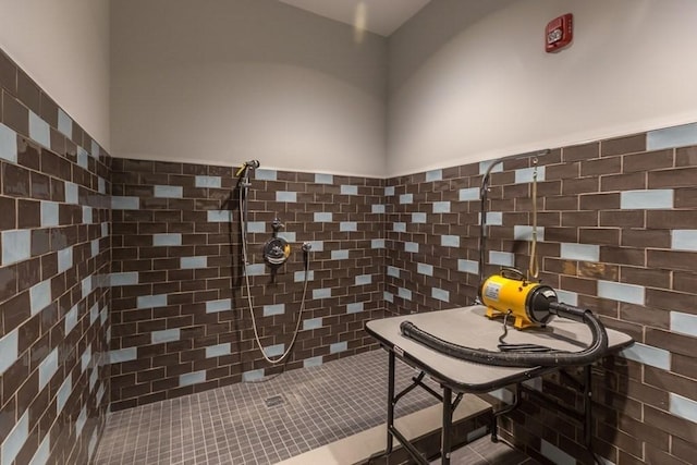 bathroom with a wainscoted wall, a tile shower, and tile walls