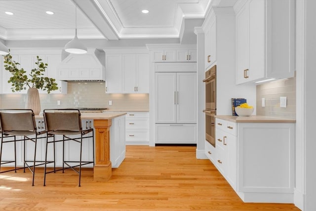 kitchen featuring premium range hood, a kitchen breakfast bar, white cabinets, light countertops, and decorative light fixtures