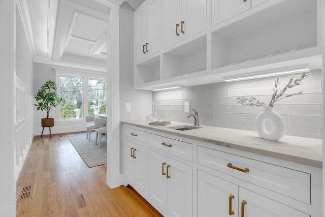 kitchen with a sink, white cabinets, backsplash, light stone countertops, and open shelves