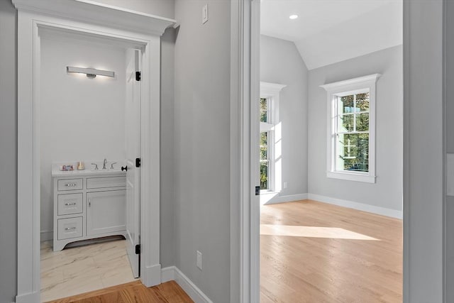 hall with light wood-type flooring, vaulted ceiling, a sink, and baseboards