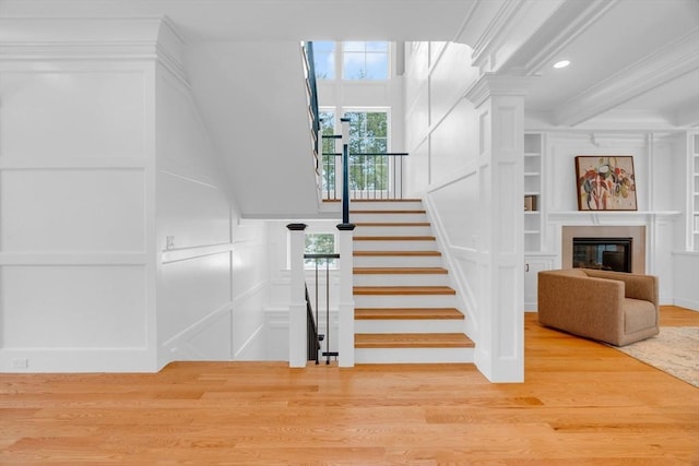 stairway featuring built in shelves, a decorative wall, a fireplace, wood finished floors, and ornamental molding