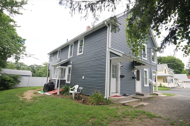 rear view of house with a lawn, fence, a chimney, and entry steps