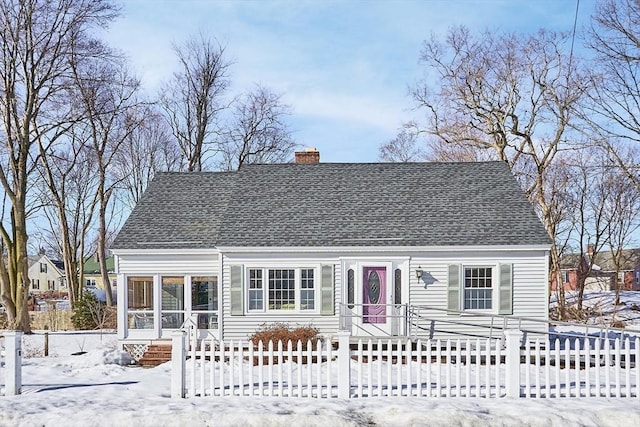 cape cod house featuring a fenced front yard, a chimney, and roof with shingles