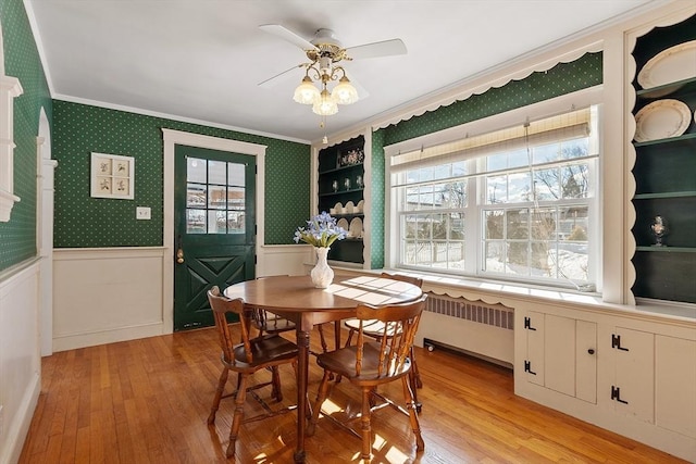 dining space with light wood-type flooring, wainscoting, wallpapered walls, radiator heating unit, and crown molding