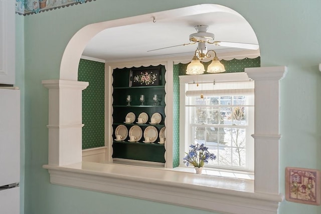 interior details featuring arched walkways, crown molding, a ceiling fan, freestanding refrigerator, and wallpapered walls