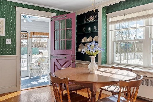 dining space featuring radiator, wallpapered walls, crown molding, and wood finished floors