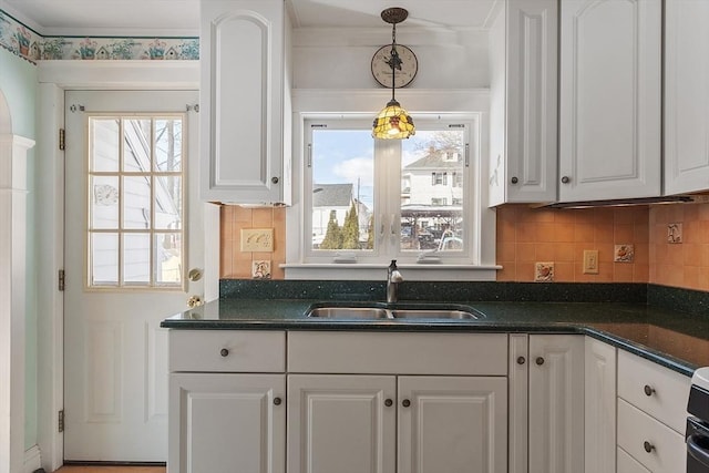 kitchen with hanging light fixtures, backsplash, white cabinetry, a sink, and dark stone countertops