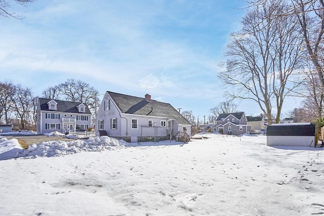 snow covered back of property featuring a chimney