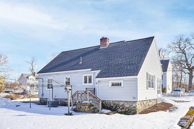 snow covered property with a shingled roof and a chimney