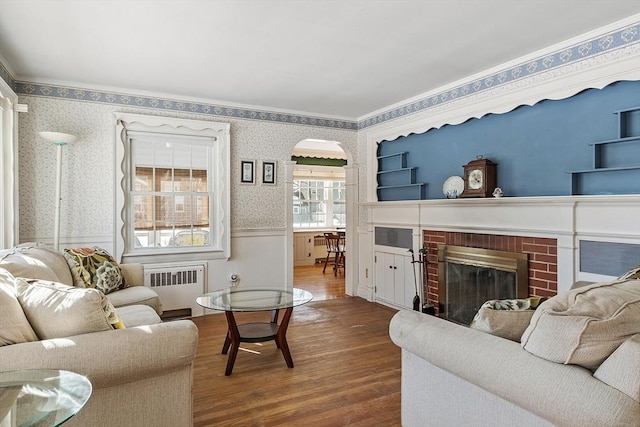 living area featuring a wainscoted wall, radiator heating unit, arched walkways, and wallpapered walls