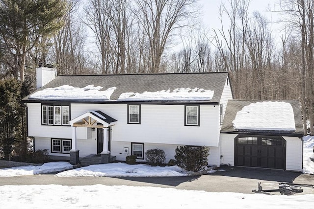 bi-level home featuring aphalt driveway, a chimney, and a garage