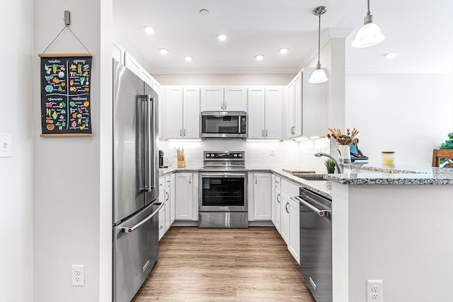 kitchen with hanging light fixtures, sink, white cabinetry, light stone counters, and stainless steel appliances