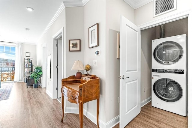 clothes washing area with stacked washer and clothes dryer, ornamental molding, and light wood-type flooring