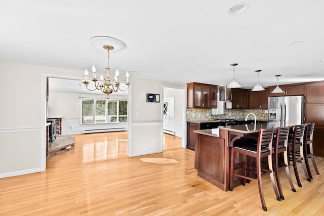 kitchen featuring stainless steel fridge with ice dispenser, decorative light fixtures, a breakfast bar, and an island with sink