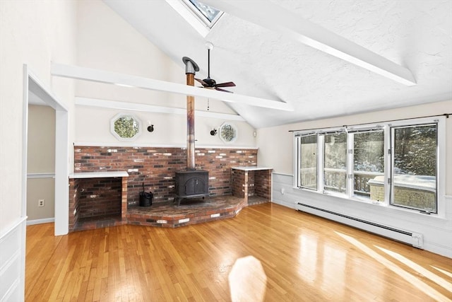 unfurnished living room featuring lofted ceiling with skylight, a textured ceiling, a wood stove, a baseboard radiator, and hardwood / wood-style floors