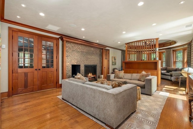 living room featuring crown molding, french doors, a brick fireplace, and light wood-type flooring