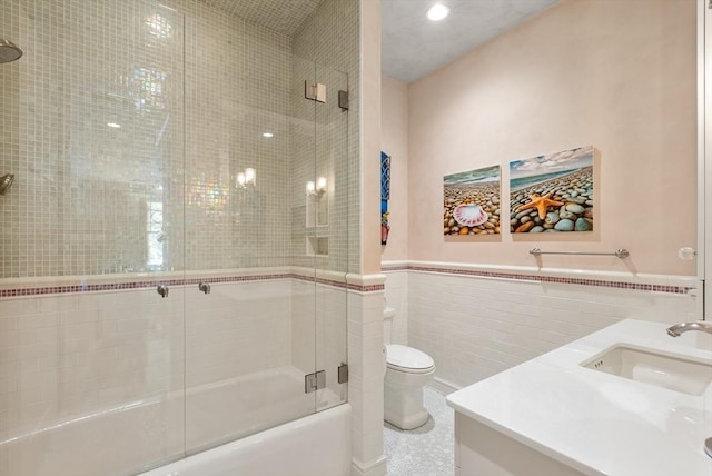 full bathroom featuring vanity, tile walls, shower / bath combination with glass door, and toilet