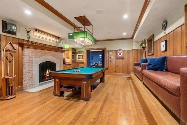 game room with ornamental molding, light hardwood / wood-style floors, a brick fireplace, and wood walls