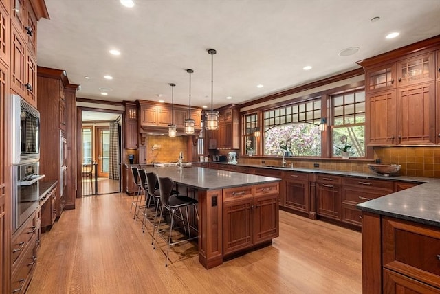 kitchen featuring pendant lighting, a kitchen island with sink, backsplash, light hardwood / wood-style floors, and built in microwave