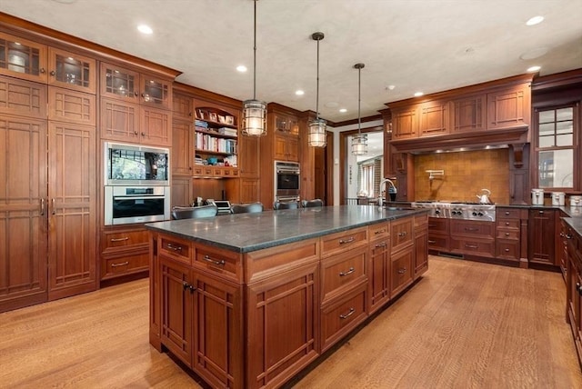 kitchen featuring black microwave, an island with sink, pendant lighting, and light hardwood / wood-style flooring