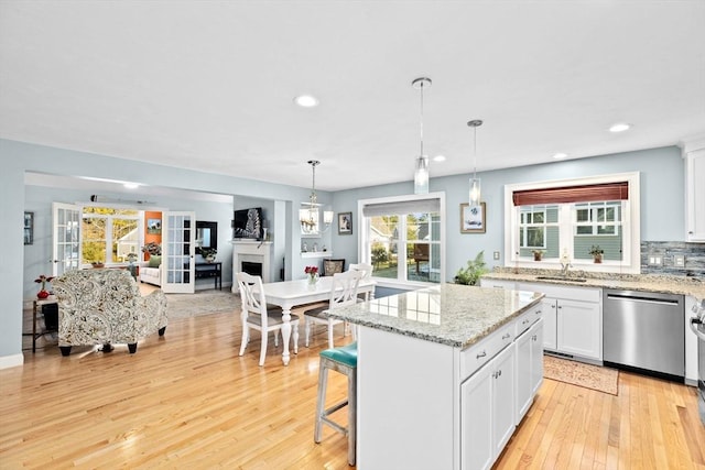 kitchen with a kitchen island, sink, white cabinets, a kitchen bar, and stainless steel dishwasher