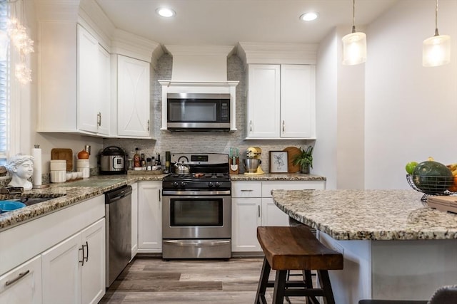 kitchen with white cabinetry, stainless steel appliances, decorative light fixtures, and a breakfast bar area