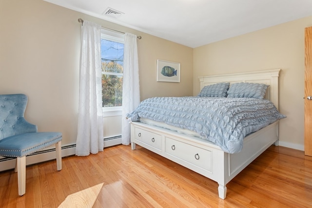 bedroom with light hardwood / wood-style floors and a baseboard heating unit