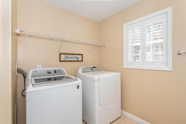 clothes washing area with light tile patterned floors, laundry area, washer and clothes dryer, and baseboards