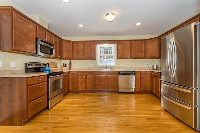 kitchen with appliances with stainless steel finishes, brown cabinets, light countertops, light wood-style floors, and a sink