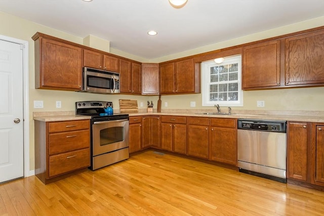 kitchen with light countertops, appliances with stainless steel finishes, light wood-type flooring, and a sink