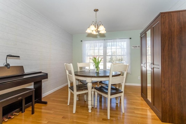 dining room with baseboards, a notable chandelier, wood walls, and light wood finished floors