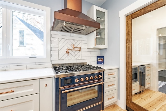 kitchen featuring high end stove, light hardwood / wood-style floors, white cabinetry, and wall chimney range hood