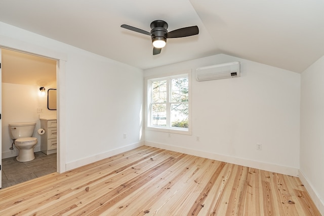 unfurnished bedroom with a wall mounted air conditioner, ensuite bathroom, vaulted ceiling, ceiling fan, and wood-type flooring