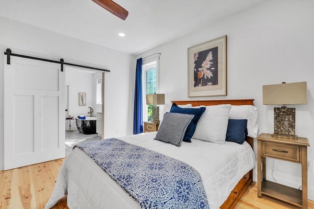 bedroom with light wood-type flooring, ceiling fan, and a barn door