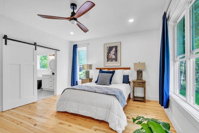 bedroom featuring ceiling fan, a barn door, wood-type flooring, and ensuite bath