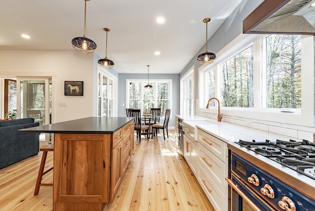 kitchen with sink, hanging light fixtures, a kitchen bar, white cabinets, and light wood-type flooring