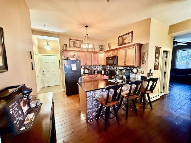 kitchen featuring dark countertops, wood-type flooring, decorative backsplash, a peninsula, and black appliances