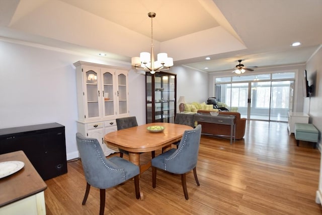 dining space with a tray ceiling, recessed lighting, light wood-style floors, ornamental molding, and ceiling fan with notable chandelier