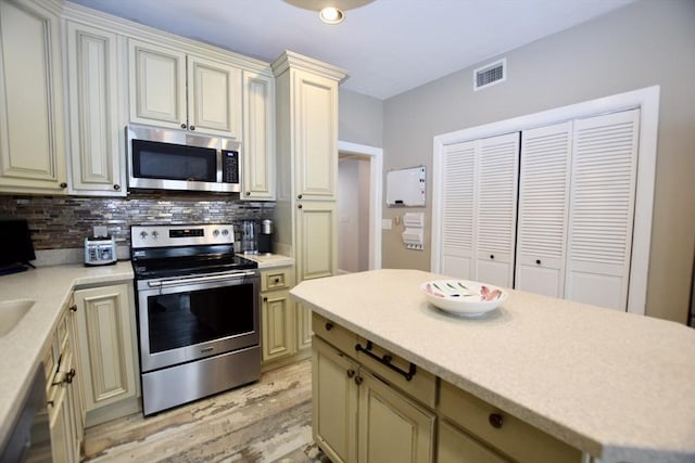 kitchen featuring light countertops, appliances with stainless steel finishes, cream cabinetry, and tasteful backsplash