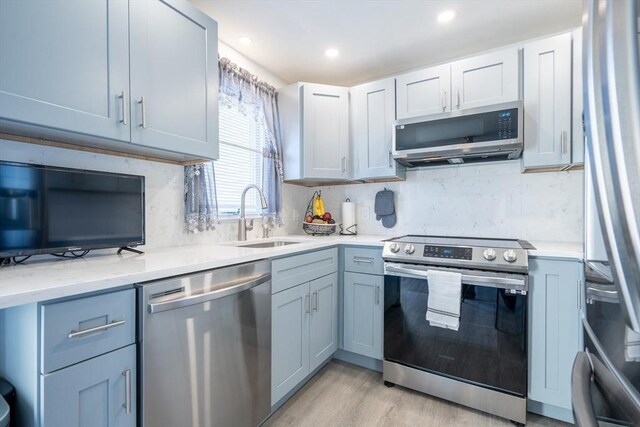 kitchen with stainless steel appliances, recessed lighting, decorative backsplash, a sink, and light wood-type flooring